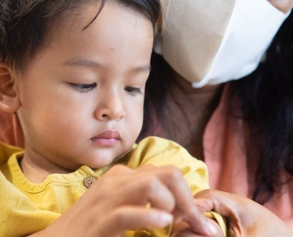Child with a rare disease wearing a yellow shirt, being held by parent